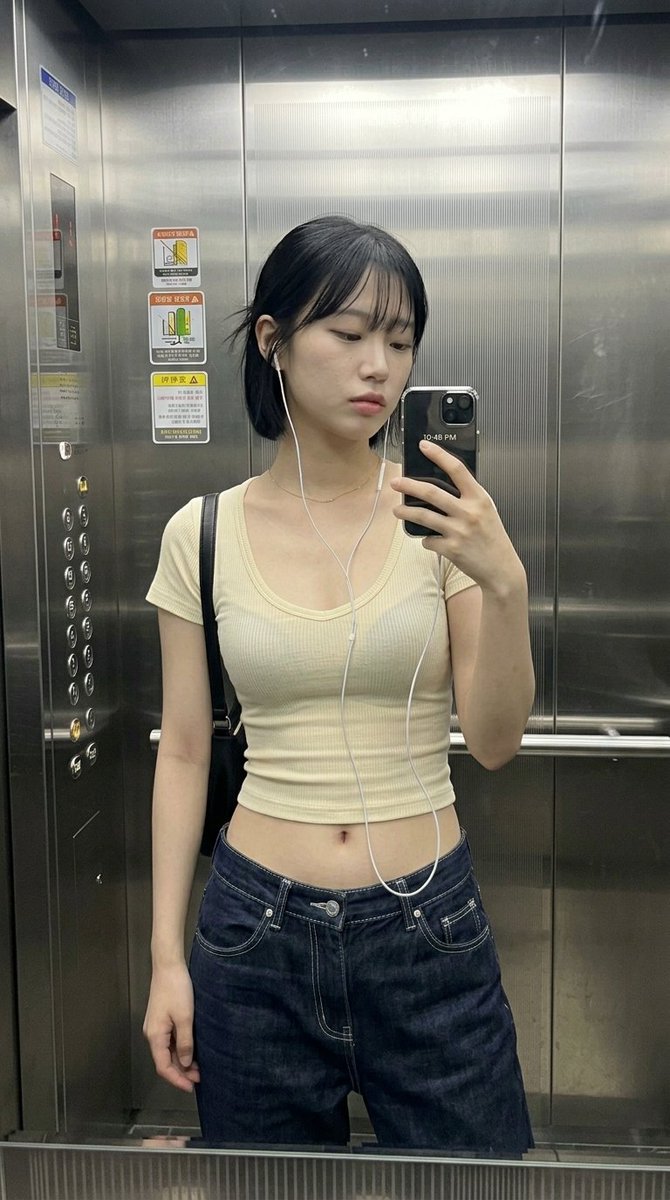 一位年轻女性在电梯里随意地对着镜子自拍。, 右手持手机，部分遮住下巴和下半张脸。, 二十岁出头, 冷漠, 平静, 看着手机屏幕, 微微张开, 中性, 放松、自然抓拍, true, 韩系休闲街头...