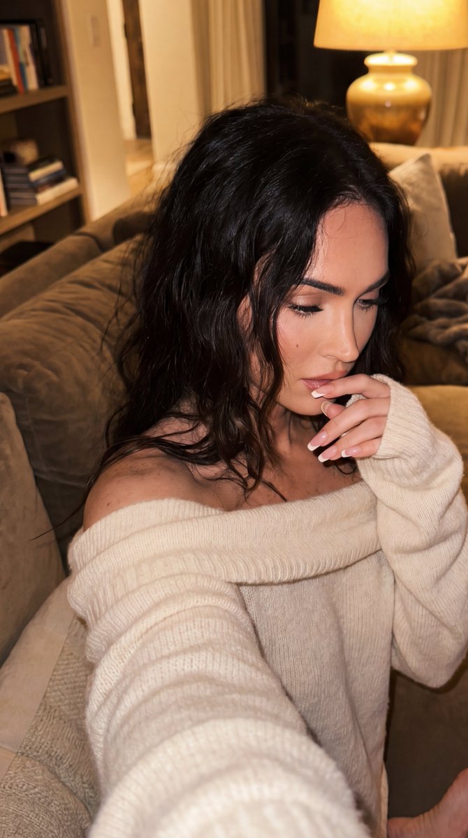 法式长指甲, 精致法式美甲足部, Megan Fox, 坐在沙发上, 一条腿收拢，一条腿略微伸展, 赤脚可见于画面边缘附近, 低垂放松的目光，柔和而有力度, 深色凌乱波浪卷, 柔软质感，宽松领...