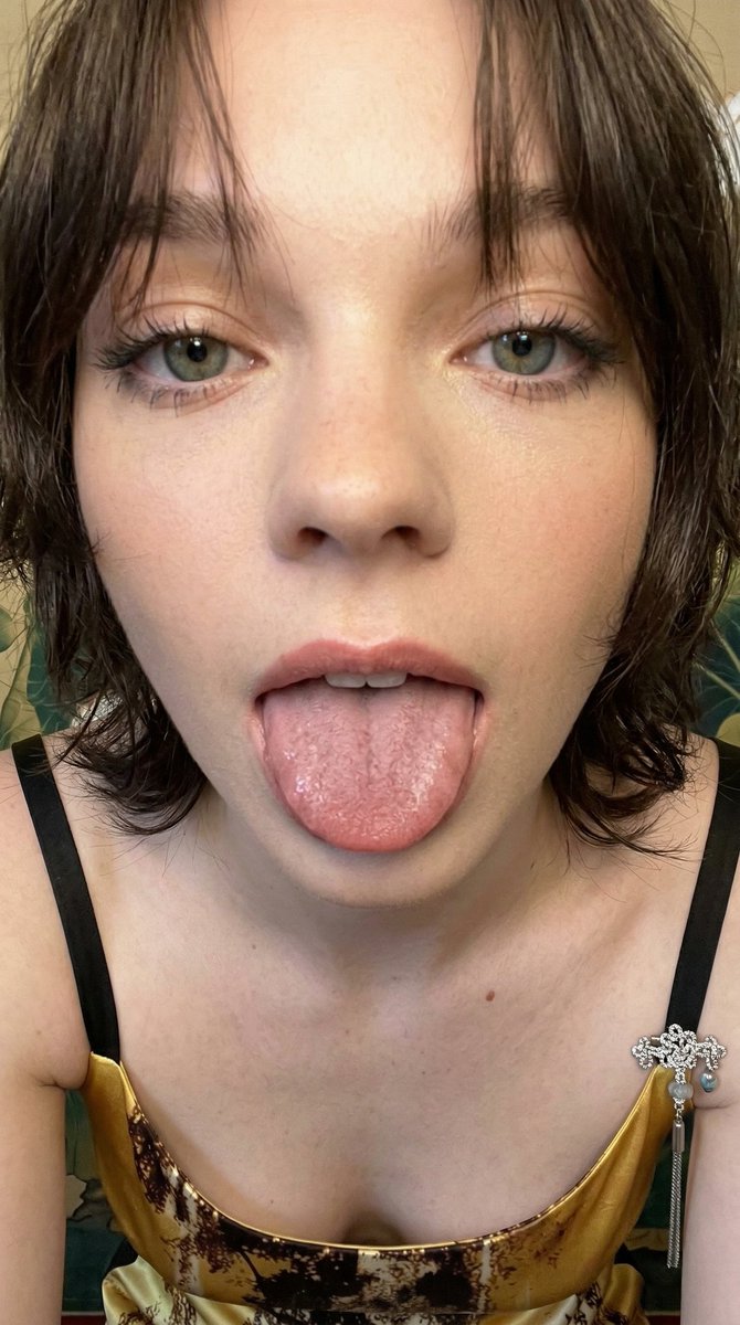 一张极近距离的智能手机业余特写肖像，捕捉到一位年轻女性面部的下半部分，她顽皮地将舌头伸向镜头。主体伸出舌头，展现出宽阔平坦的肌肉表面，布满细密的丝状乳头，并带有微微的湿润光泽。她的双唇微微张开...