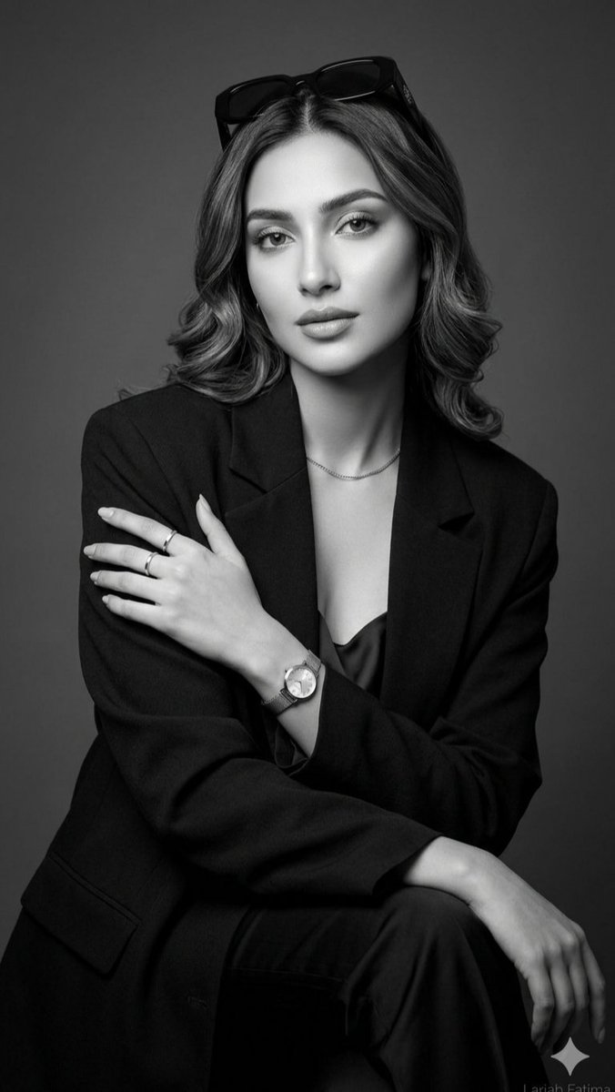 一张精致的黑白摄影棚人像照,画面中是一位举止从容优雅的年轻女性。她身穿剪裁考究的黑色西装外套,内搭丝绸吊带背心,头顶时尚地架着一副深色太阳镜。她柔软蓬松的头发被梳理成波浪卷。她佩戴着简约奢华的...