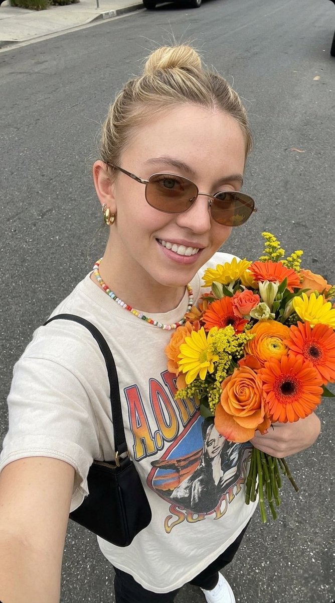 超现实自拍照片，一位年轻女子手持一束新鲜花束， 姿势：俯拍自拍角度，将花束贴近胸前，浅浅微笑，自然放松的表情， 外观：肌肤洁净有光泽，头发整齐地盘成发髻，柔和自然妆容，唇部水润亮泽， 服装：休...