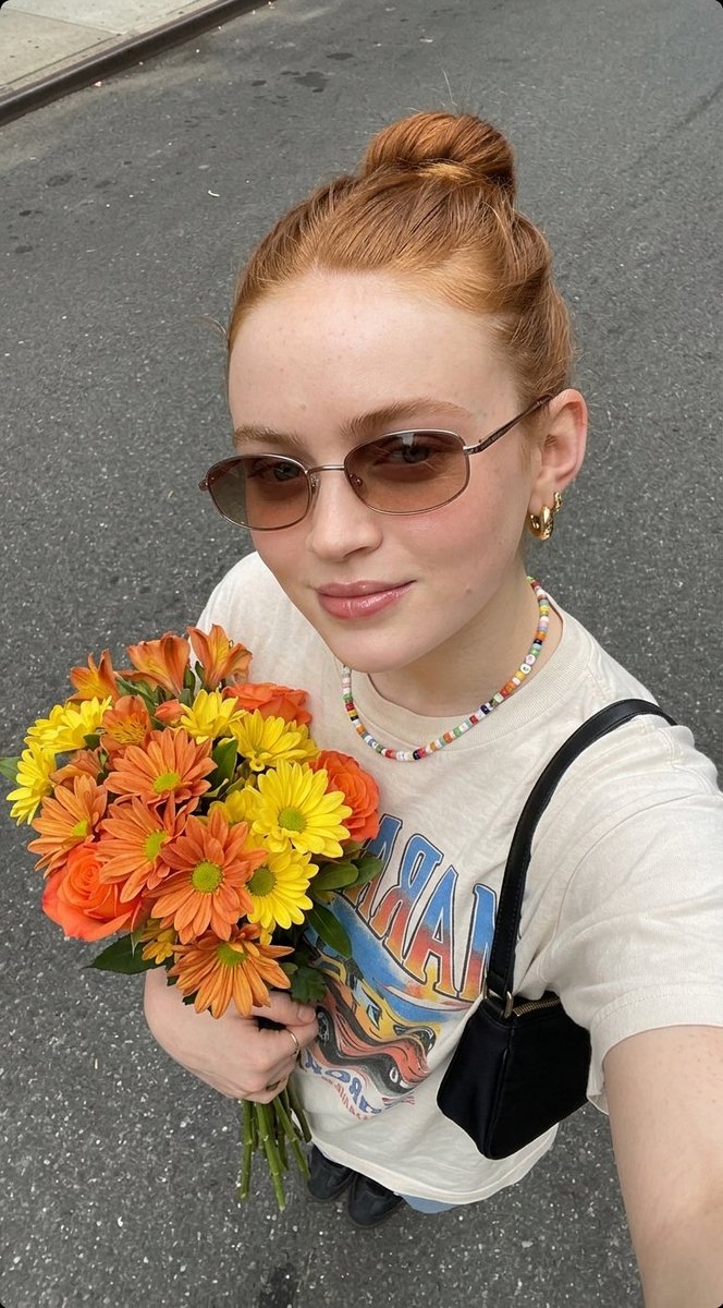 超现实自拍照片，一位年轻女子手持一束新鲜花束， 姿势：俯拍自拍角度，将花束贴近胸前，浅浅微笑，自然放松的表情， 外观：肌肤洁净有光泽，头发整齐地盘成发髻，柔和自然妆容，唇部水润亮泽， 服装：休...