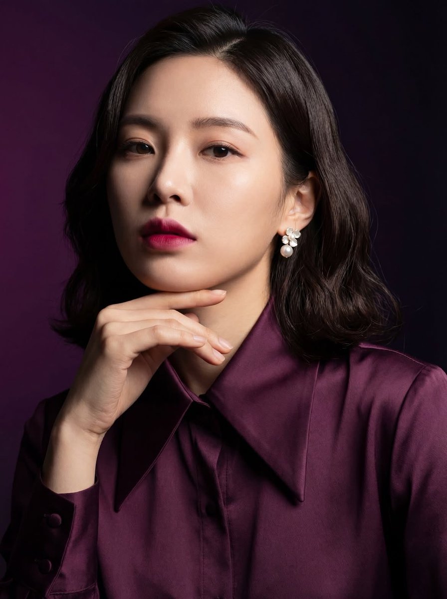 "一张优雅东亚女性的影棚肖像，肩长的深色头发，身着深梅紫色缎面衬衫，柔和自然的妆容搭配大胆的粉色唇彩，佩戴珍珠花卉耳环，手轻托下巴，神情自信而沉静，皮肤光滑无瑕，戏剧化的柔和光线配以细腻的阴影...