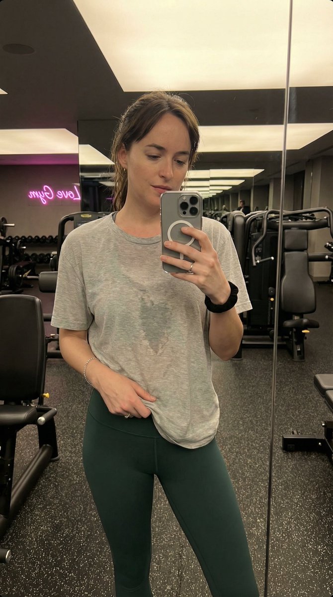 现代健身房内 Madelyn Cline 的写实风格、高度精细的抓拍式智能手机镜面自拍。她拥有运动型、曲线优美且健美的身材，腰部线条分明。她穿着一件薄的、宽松的浅蓝色短袖 T 恤，因运动后略微...
