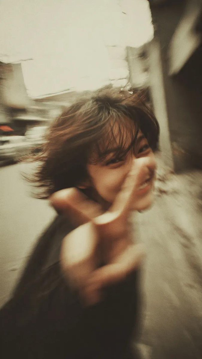 一张千禧年(Y2K)风格的街拍人像写真:一位开朗的年轻女性,留着凌乱的短波波头(bob),自然地开怀大笑,直接对着镜头比出胜利手势(V字手势/peace sign),她伸出的手占据前景,带有夸...