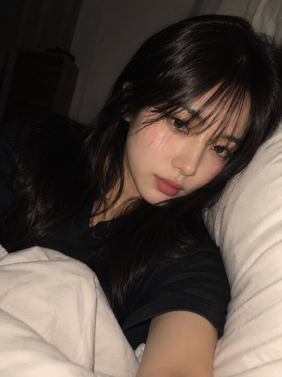 一张高度写实、亲密的夜间卧室自拍，照片中一位年轻成年东亚女性舒适地躺在床上，以一种随意、自发的智能手机拍摄方式捕捉，拍摄于即将入睡的时刻。请使用...