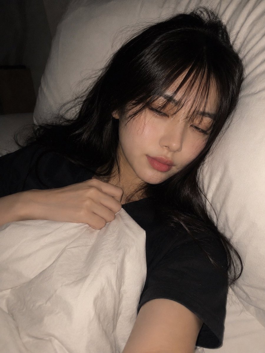 一张高度写实、亲密的夜间卧室自拍，照片中一位年轻成年东亚女性舒适地躺在床上，以一种随意、自发的智能手机拍摄方式捕捉，拍摄于即将入睡的时刻。请使用上传的图片作为面部和外貌参考，保持相同的面部结构...