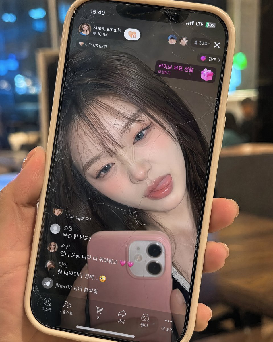 完全保留参考图片中韩国女性的面孔——不要改变她的脸型、眼睛、鼻子、嘴唇、比例、肤质或整体身份。制作一张超写实的9:16特写，画面中是一只从右侧伸出的右手握着的米色硅胶壳iPhone，占据画面大...