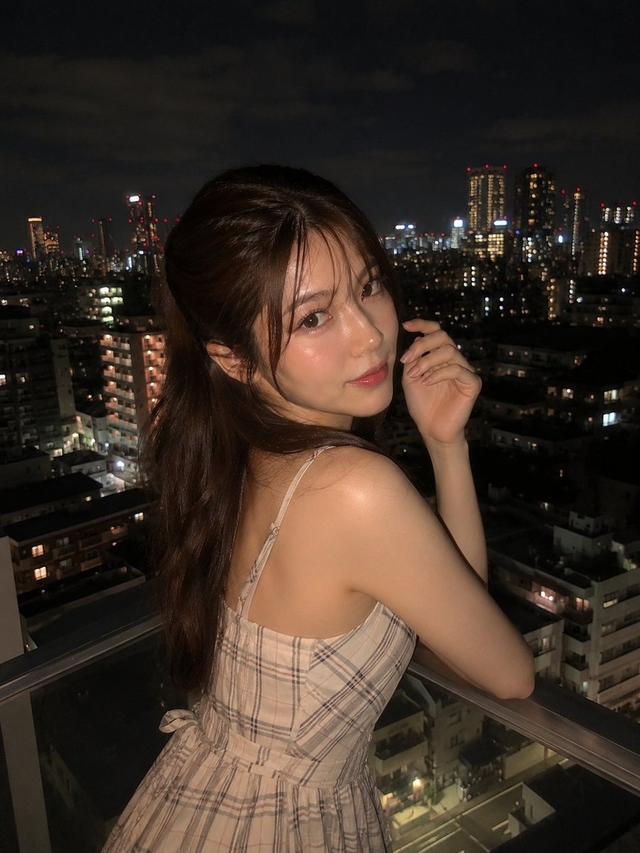 超写实夜景人像：一位美丽的年轻女子站在阳台上，俯瞰城市天际线，身穿优雅的无袖米色格纹连衣裙，淡雅腮红妆容，自然水润唇妆，慵懒的半扎发造型，几缕碎发自然垂落于脸颊两侧。她回眸望向镜头，神态温柔，...