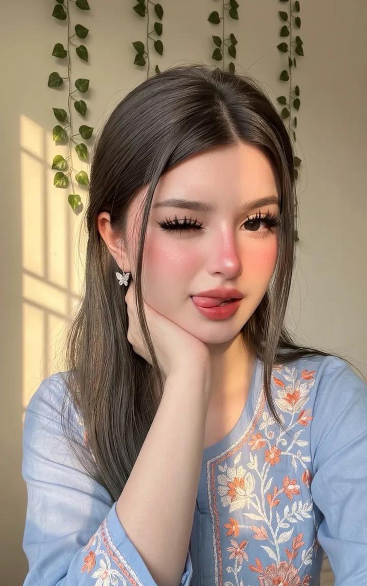 请原样保留她原有的面部特征。她天生容貌美丽，面部对称性完美。她应显得年轻且有女性魅力，拥有自然丰满的胸部，而非平坦的胸部。 这是一张室内特写自拍照，照片中是一位年轻女性，面容柔和甜美，由温暖的...