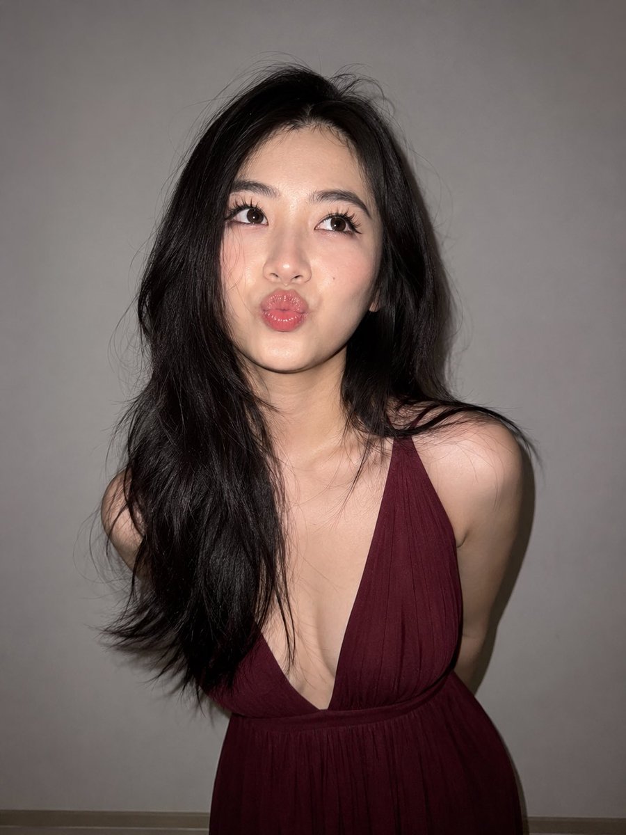 ChatGpt 图像 #chatgp 提示词 ~ 一张超写实的近距离闪光灯人像照，主体是一位年轻成年东亚女性，站在纯浅灰色墙壁前。她有一头浓密的乌黑长发，带有柔和的自然波浪和细微的飞扬发丝；肌...