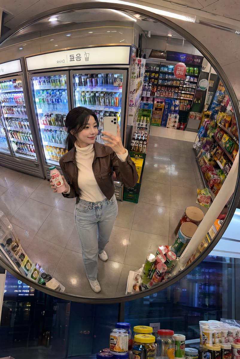 深夜韩国便利店镜面抓拍 创建一张逼真的生活方式照片，透过安装在韩国一家温馨便利店天花板上的一面大型凸面镜拍摄，场景为夜晚。画面中一位时尚的年轻韩国女性从略微抬高的镜面视角被捕捉到，她正在冷藏饮...