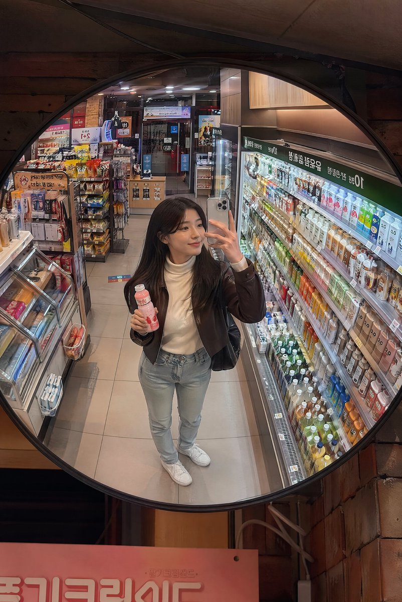 深夜韩国便利店镜面抓拍 创建一张逼真的生活方式照片，透过安装在韩国一家温馨便利店天花板上的一面大型凸面镜拍摄，场景为夜晚。画面中一位时尚的年轻韩国女性从略微抬高的镜面视角被捕捉到，她正在冷藏饮...