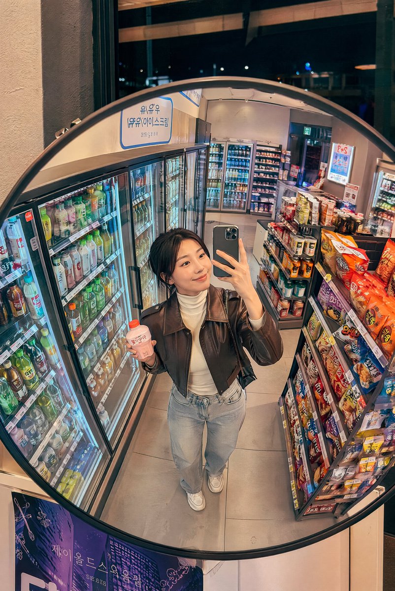 深夜韩国便利店镜面抓拍 创建一张逼真的生活方式照片，透过安装在韩国一家温馨便利店天花板上的一面大型凸面镜拍摄，场景为夜晚。画面中一位时尚的年轻韩国女性从略微抬高的镜面视角被捕捉到，她正在冷藏饮...