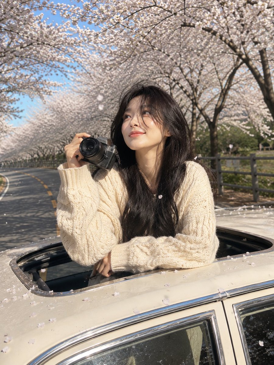 梦幻春日旅行人像：一位年轻女子从一辆白色复古汽车的电动天窗探出身来，手中握着一台相机。乌黑长发飘逸自然，妆容柔和自然，肌肤透亮，神态平静而若有所思。身穿一件米白色超大款针织毛衣，质感温暖舒适。...