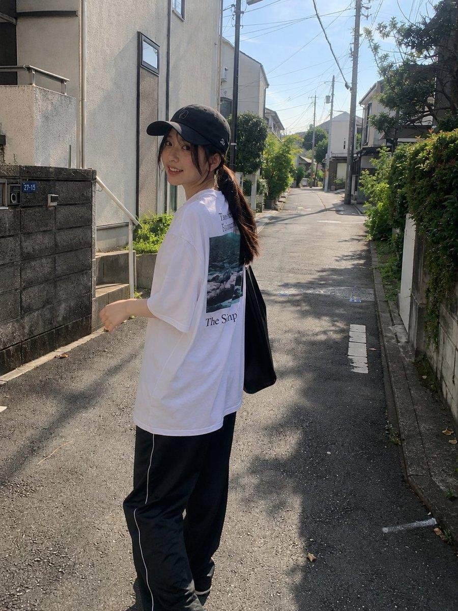 漂亮的年轻日本女孩,肌肤白皙,妆容柔和自然,深色长发在黑色棒球帽下扎成低马尾,身穿宽松的白色印花T恤和黑色宽松全长运动裤。在一个晴朗的午后,她随意地走过一条安静的住宅小巷,一只手自然地举到脸旁...