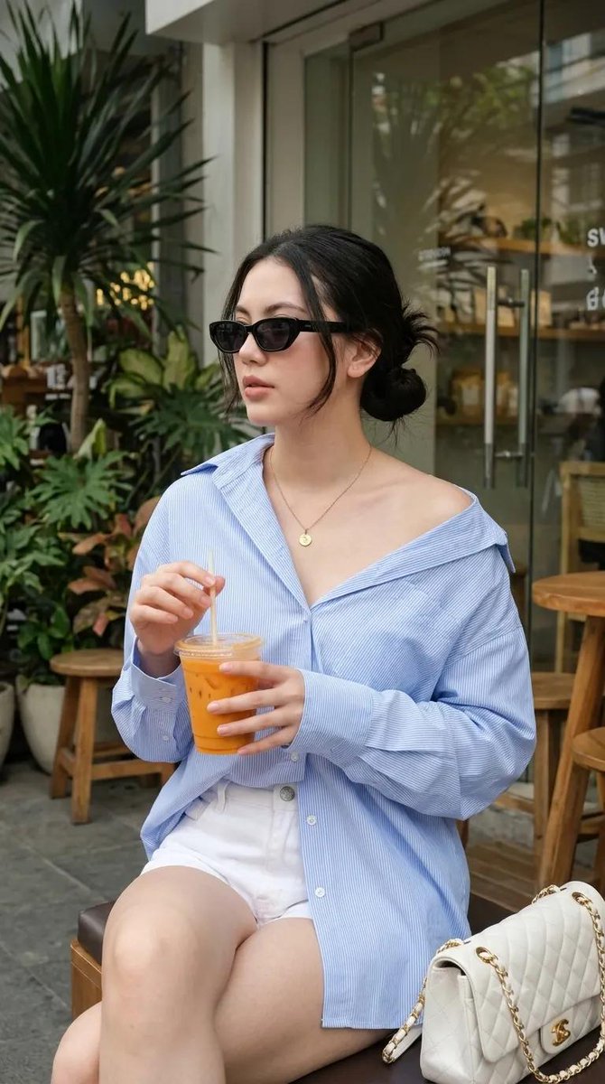 使用我的图片，生成一张 9:16 的图像 --- 一位年轻女性坐在户外咖啡馆，随性慵懒的 Oversized 风格。身穿宽松 Oversized 浅蓝色细条纹纽扣衬衫，袖子卷起，衬衫垂落足够长...