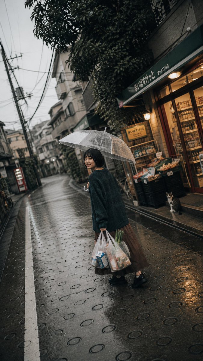 一张电影感、怀旧风格的生活方式摄影作品，拍摄于日本雨后湿漉漉的住宅街道上。一位年轻日本女性留着黑色短款波波头，站在道路中央，温柔地微笑着回头望向镜头。她单手撑着一把透明雨伞举过头顶，另一只手提...