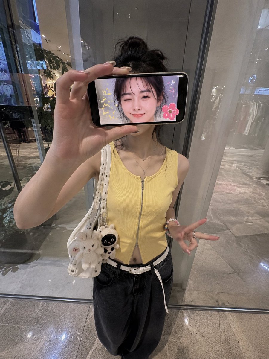 超现实创意iPhone人像照：一位时尚的日本女性站在现代购物中心的反光玻璃墙前，采用略微抬高的正面拍摄角度，呈现0.5x iPhone广角镜头美学。 她横向握着一部智能手机放在脸前，完全遮住眼...