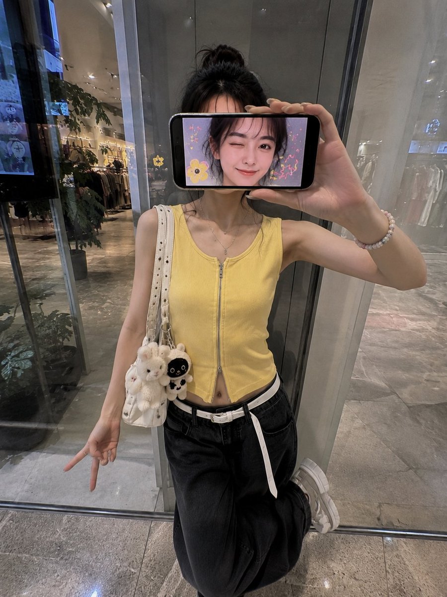 超现实创意iPhone人像照：一位时尚的日本女性站在现代购物中心的反光玻璃墙前，采用略微抬高的正面拍摄角度，呈现0.5x iPhone广角镜头美学。 她横向握着一部智能手机放在脸前，完全遮住眼...