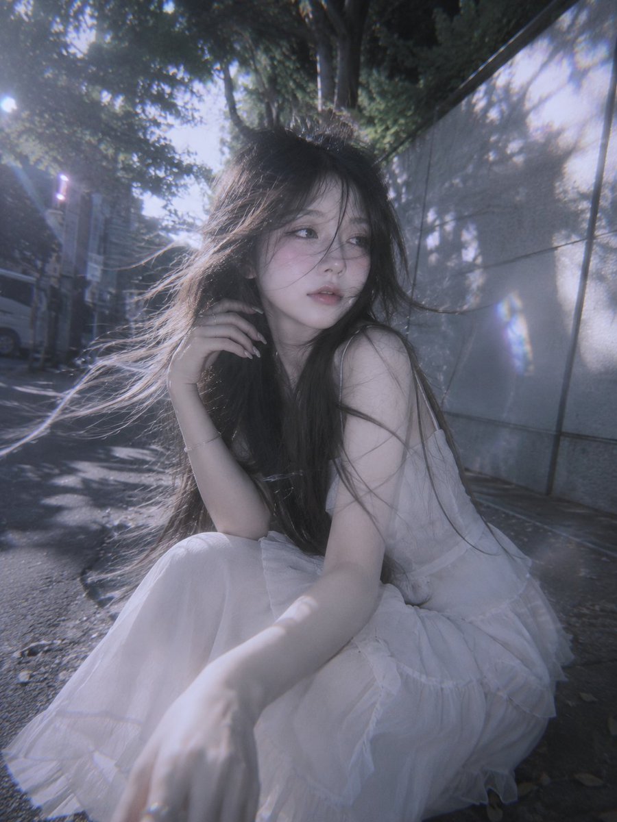 一位超现实的、如同人偶般的年轻女性，留着及腰的飘逸长发，以真实自然的抓拍肖像呈现，散发出柔和的日常魅力。她看起来有些害羞，但与镜头之间有一种温柔的联结，微风轻拂，发丝自然地在她脸庞周围飘动。她...