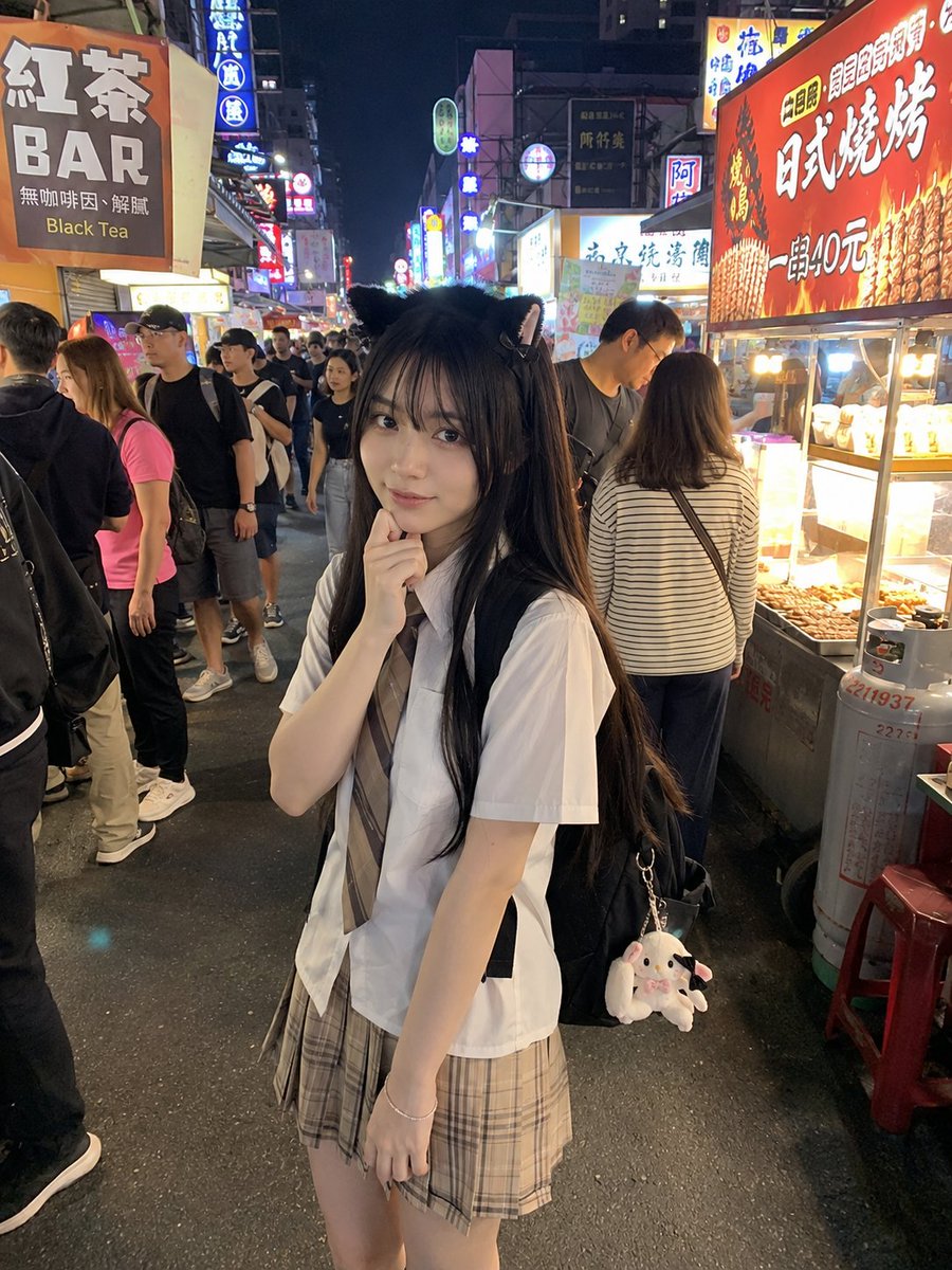 年轻的日本女孩，留着顺直黑色长发和柔软的刘海，戴着可爱的黑色猫耳发箍，身穿白色短袖衬衫、条纹领带和米色格纹百褶裙。她站在一个充满活力的亚洲夜市里，四周是霓虹招牌、美食摊位和熙熙攘攘的人群。她一...