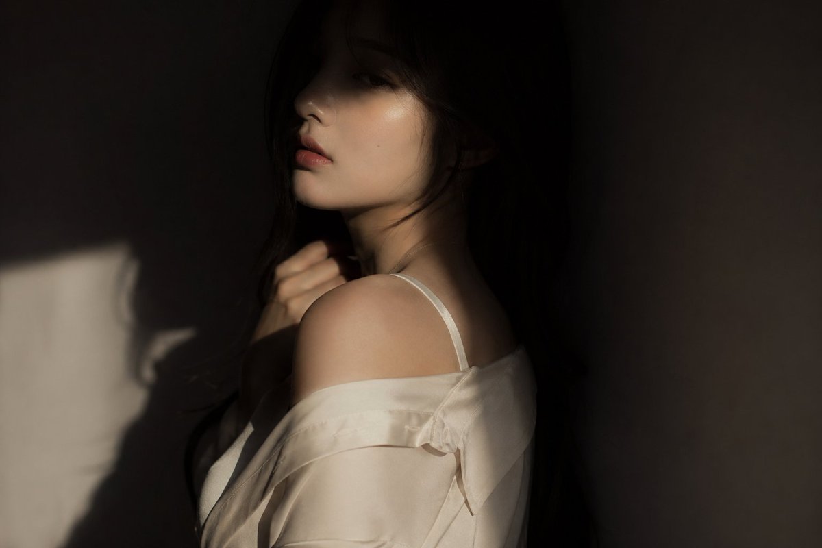 电影感编辑风格人像：韩国女团偶像，氛围微妙而迷人 服装：略宽松的真丝或柔软面料上衣，优雅且流动 姿势：躯干背向镜头，脸部仅部分可见，一只手抬起靠近领口或喉咙 表情：柔和而神秘，双眼半隐 光线：...