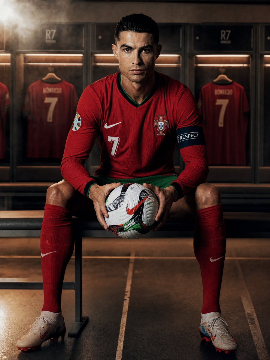 创作一张超写实的摄影作品：[team]球队的[footballer]坐在更衣室里，手持一个足球，全身正面视角，目光直视镜头。球员身穿官方球队球衣。戏剧性的侧光配以强烈阴影，背景中虚化的金属储物...