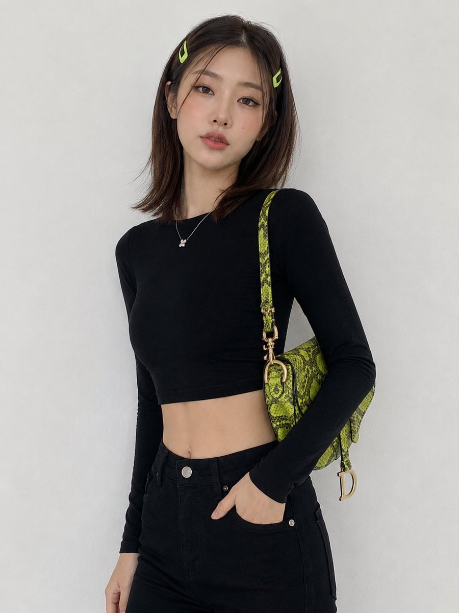 创建一幅图像：一位年轻韩国女性，中长棕色头发，两侧别着青柠绿色发夹，倚靠在一面纯白色墙壁前摆姿势，身穿黑色短款长袖上衣、黑色高腰长裤，肩上斜挎一款色彩鲜艳的青柠绿色蛇纹鞍形包。