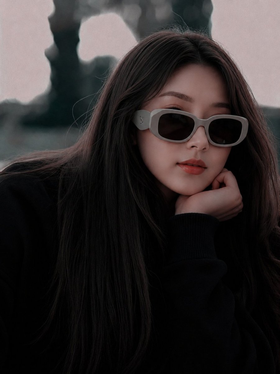 超现实电影级时尚人像:一位美丽的年轻东亚女性,长直深棕色头发,身穿超大黑色毛衣,佩戴厚重的哑光灰色奢侈品牌设计师太阳镜。她将下巴轻搁于手上,神情平静地望向镜头,拥有柔和自然的唇色和无瑕瓷肌。淡...