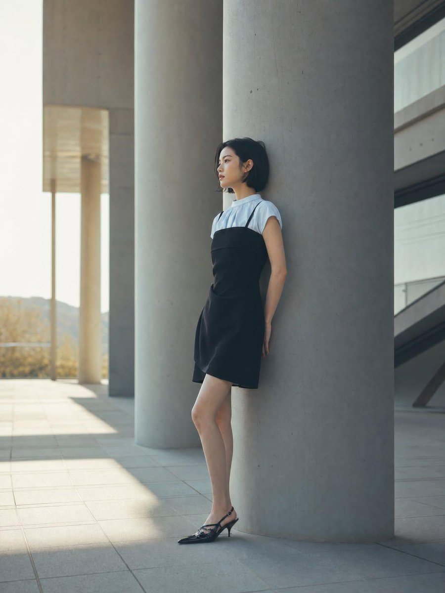 一位身材纤细的年轻女性，留着黑色短波波头发型，靠在现代建筑广场上一根巨大的混凝土柱上，身穿黑色吊带裙内搭白色短袖上衣，脚踩黑色尖头后跟凉鞋，妆容自然柔和，侧脸若有所思，极简时尚大片，宏伟的混凝...