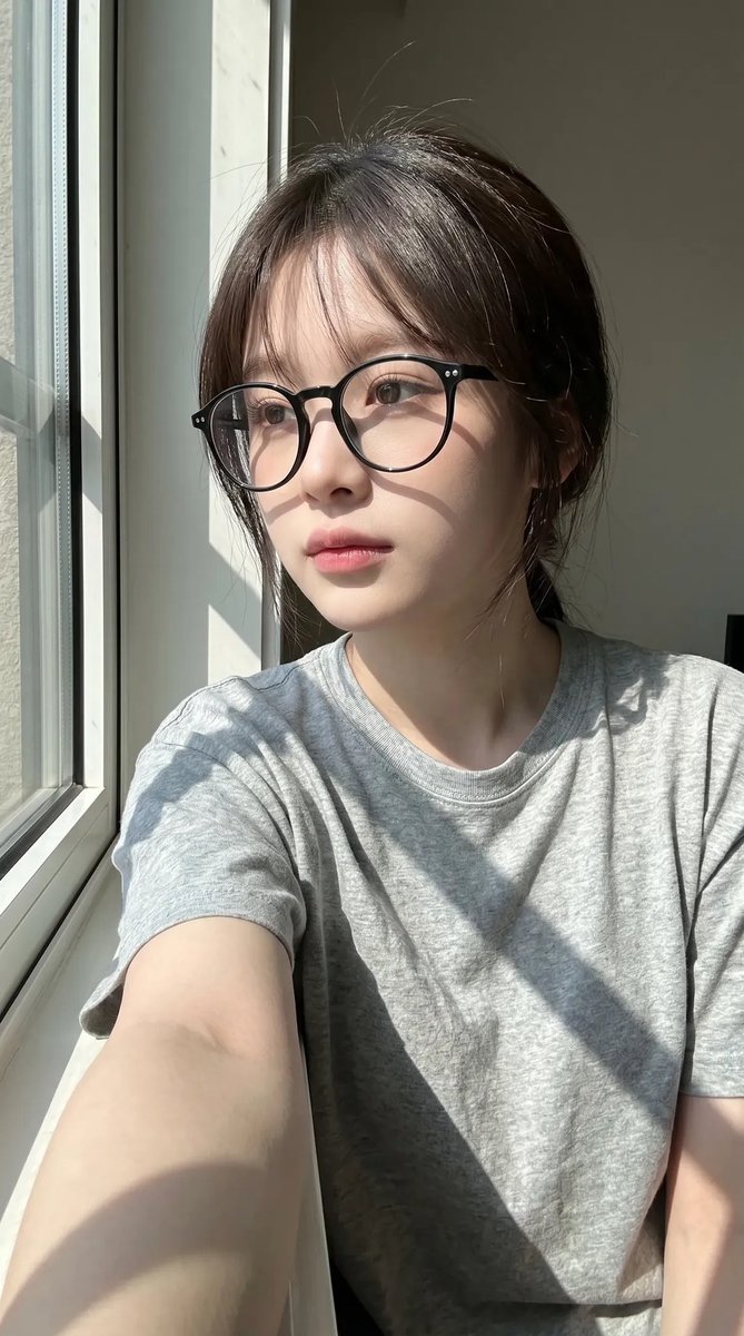 超写实抓拍式智能手机自拍照肖像：一位年轻东亚女性室内坐在一扇大窗户旁，处于明亮的自然日光下。保持与上传的面部参考高度相似的面部特征：柔和的椭圆形脸型、纤细的下颌线、自然偏窄的鼻梁、轮廓轻柔的嘴...