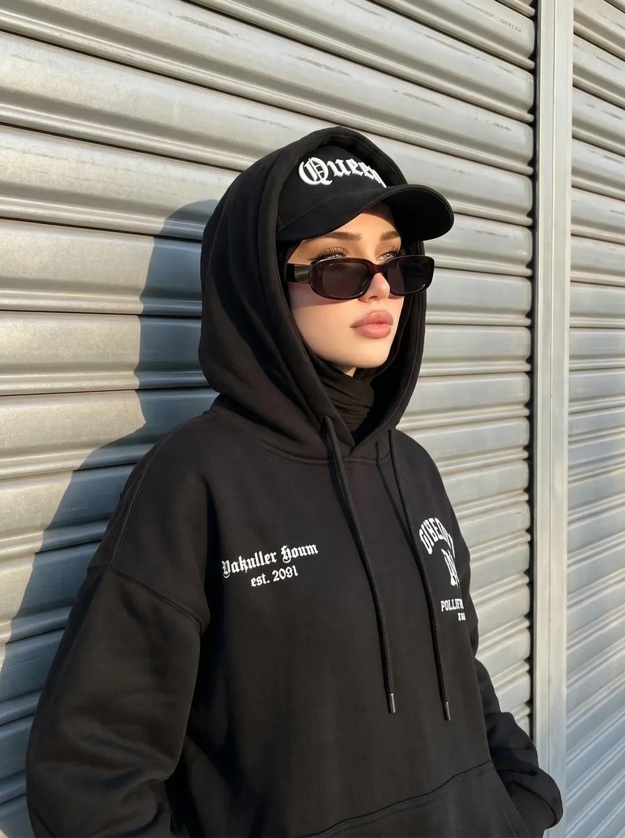 创建一张与所附参考图片具有完全相同面部特征和特征的图像，不改变任何特征。 一张街头风格的头巾女性肖像，她有着冷酷前卫的气质。她戴着黑色头巾，一件胸前印有白色文字的超大黑色连帽卫衣外套，以及一顶...