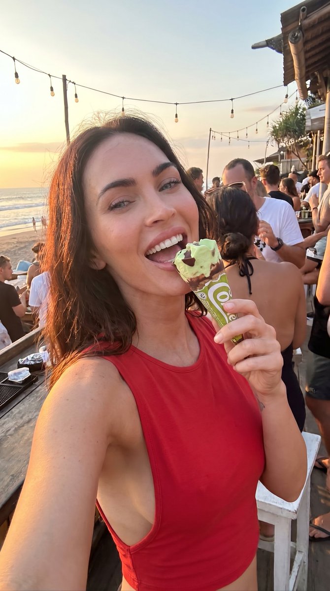 业余特写微模糊自拍的美味惊艳意大利瘦削棕发女友 emily ratajkowski，正在舔食一个草莓奶油甜筒(cornetto gelato)，并在日落时分一家繁忙的酒吧里大笑。自然蓝色眼睛直...