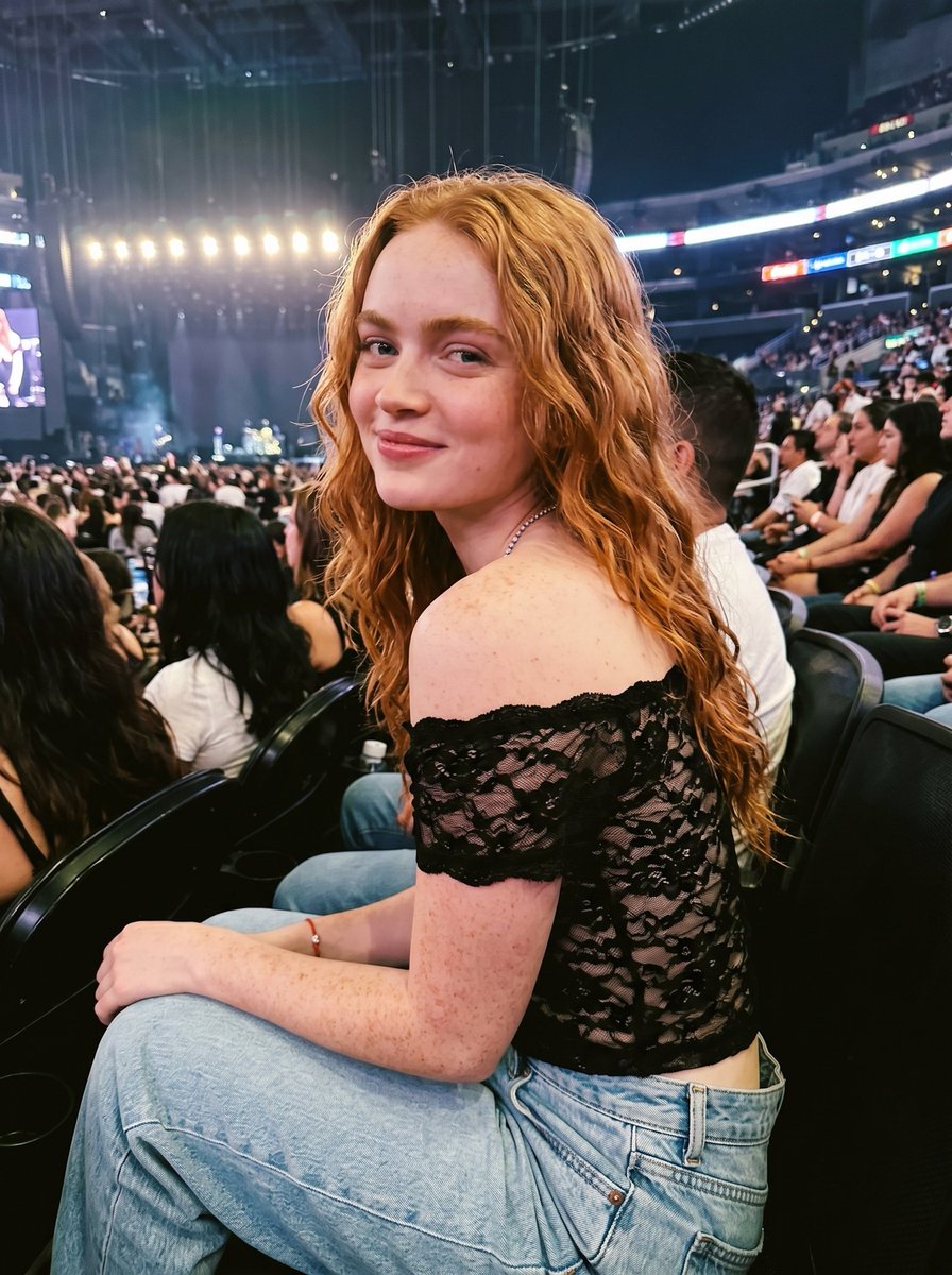 一位美丽的年轻女性 [ Sadie Sink ]，拥有波浪状的长姜红色头发，白皙的皮肤上自然分布着雀斑，覆盖在面部、肩膀和手臂上，明亮的蓝色眼睛，带着温柔的微笑。她身穿一件黑色露肩蕾丝短款上衣...