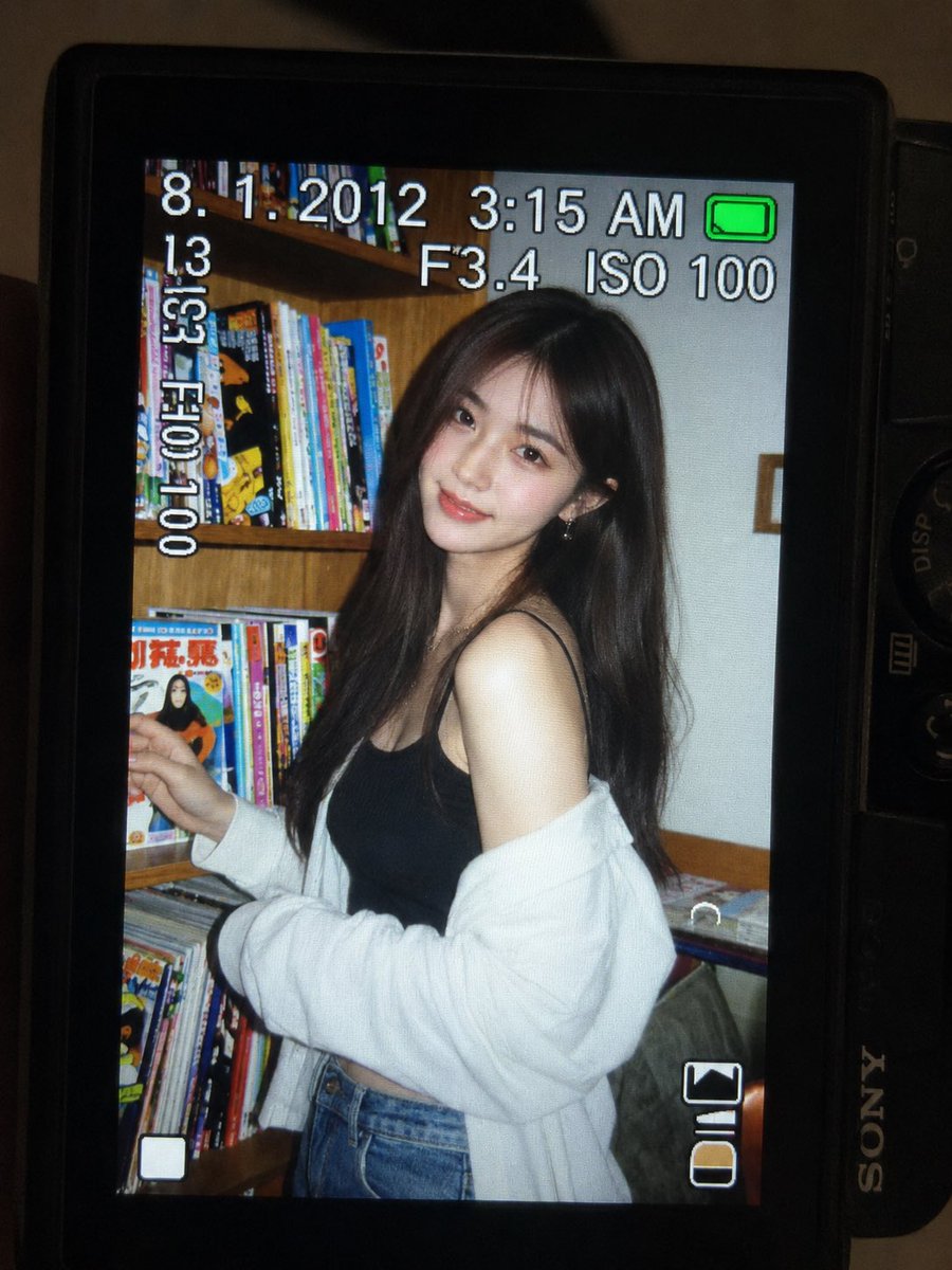 一张超精细的特写镜头：一台微型紧凑型数码相机的 LCD 屏幕在原本黑暗的室内房间中明亮发光。屏幕上是一张 2010 年代初期的随性傻瓜相机快照，画面中一位年轻东亚女性留着一头深色长波浪卷发，站...