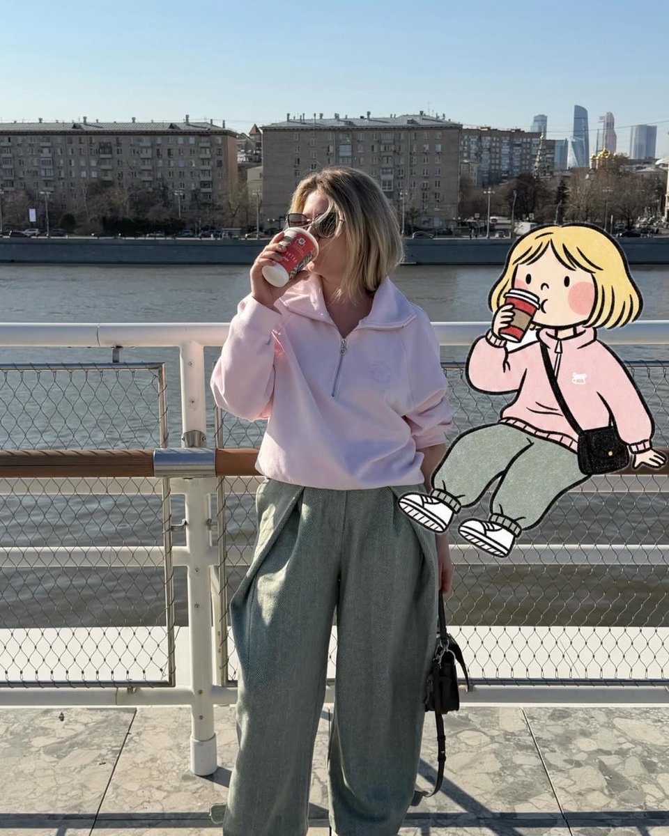 柔和的抓拍街头摄影,一位时尚女性站在河边渡轮甲板上,手持红色外带杯喝咖啡,晴朗午后光线,柔和粉彩色调,超大浅粉色半拉链卫衣,宽松灰色长裤,黑色单肩包,金色短波波头发型,戴着墨镜,背景为城市天际...