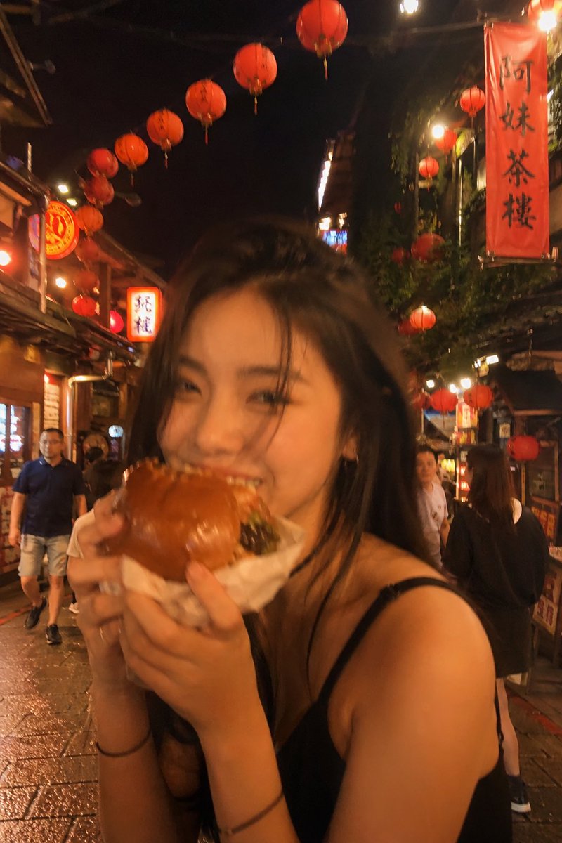 失焦的业余快照：一位亚洲超级模特站在夜晚的老台湾街道中央，发光的红灯笼照亮了整个场景。她坐在街边小吃桌前，吃着一个多汁的大汉堡，心情愉悦。暖色调。Pinterest 美学。JPG。 #AIar...