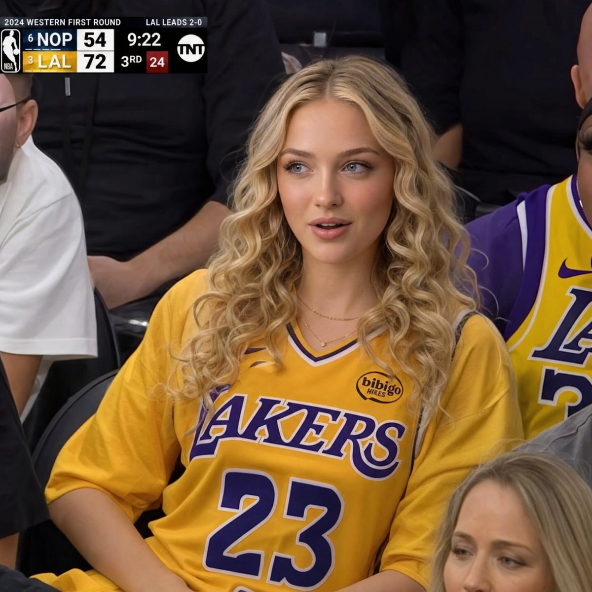 超逼真的NBA电视直播画面, 保留参考图像中的确切身份, 坐在球馆观众席中的年轻女性, 惊讶的被抓拍反应,嘴唇微微张开, 身体微微后仰,姿态放松,一只手臂搭在椅子或腿上, 宽松的金色洛杉矶湖人...