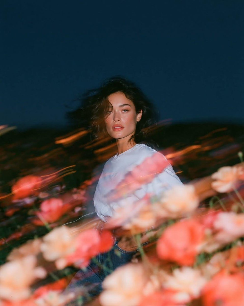 写实风格的实验性时尚人像：一位天生丽质的年轻女子正面站立于蓝色时刻狂风拂过的野花田中，镜头从大腿向上以平视取景。她身穿一件宽松的纯白棉质T恤，搭配水洗中蓝色直筒牛仔裤，日常随性的自然穿搭，深色...