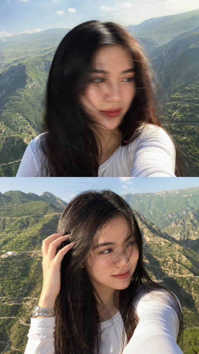 一张梦幻电影感的自拍照：一位美丽的年轻女子站在山顶观景点，长发笔直乌黑，拍摄于黄金时刻。她身穿一件修身白色长袖上衣，佩戴一只银色金属腕表。微风轻轻吹动她的头发拂过面庞，她柔和自然地望向镜头之外...