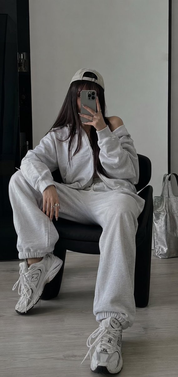以我上传的照片作为面部参考。 使用 iPhone 拍摄。 在一个极简、明亮的房间里拍摄的一张摆拍镜子自拍照。一名年轻女子随意地坐在一把低矮的黑色...