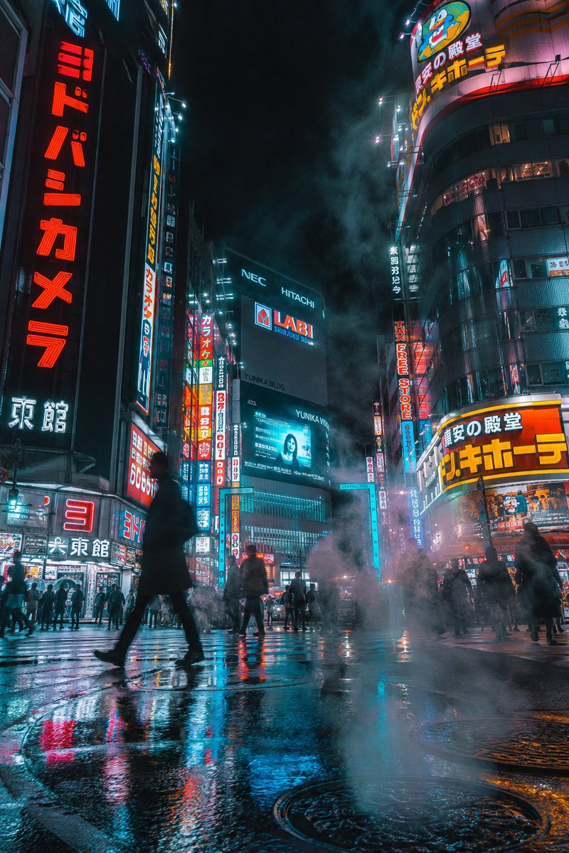夜晚的未来赛博朋克城市街道，竖向构图。霓虹招牌（包含清晰的日文文字）在高耸的摩天大楼上发光。湿润的人行道倒映着鲜艳的灯光与全息广告。浓重的蒸汽从下水道井盖升起，融入霓虹照亮的雾气中，光束穿过雾...