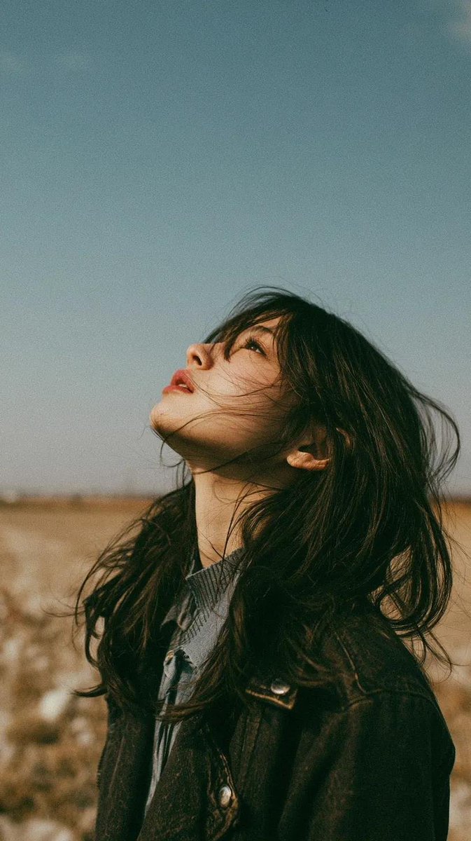 电影极简风格人像：一位美丽的年轻东亚女性独自站立在一片开阔的野花草地上，头顶是无尽的蓝天，她微微仰头，双眼或闭或半睁，仿佛在拥抱风。黑色长发自然...