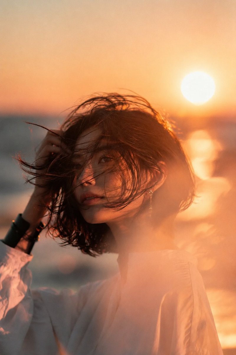 海滩日落中的美丽年轻亚洲女性，中景电影肖像。深色短发波波头在海风中飘扬，头部微向左倾，手正在整理头发。甜美浪漫的瞬间。精致优雅的耳饰，简约宽松的...