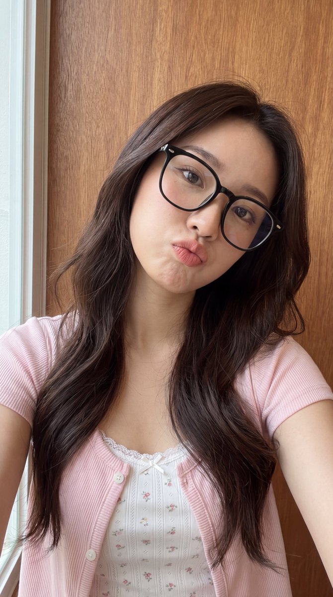 [Higgsfield 营销工作室图像提示] ar 9:16 4K High 一位年轻东亚女性的近距离自拍肖像，长长的波浪状深棕色头发垂落在一边肩膀上。她戴着一副大号黑框眼镜，俏皮地撅起嘴唇做...