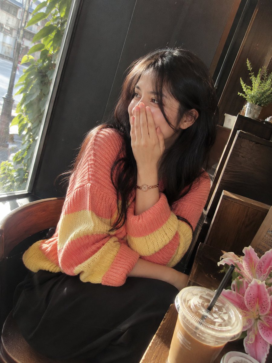 照片级写实风格的影院感咖啡馆肖像：一位美丽的成年女性，留着长而自然卷曲的深棕黑色头发，皮肤柔和泛光，五官精致，眼神富有表现力。她身穿宽松舒适的针...