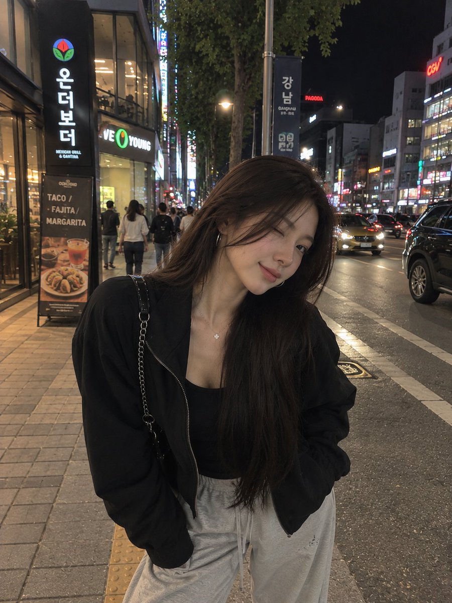 一张照片级写实风格的夜间街头人像照,一位年轻女子在繁华的韩国城市街区中随意地自拍。她留着长而顺直的黑发,妆容柔和自然,佩戴着低调的环形耳环和一条精致的项链。她身穿黑色修身内搭,外搭一件宽松的黑...