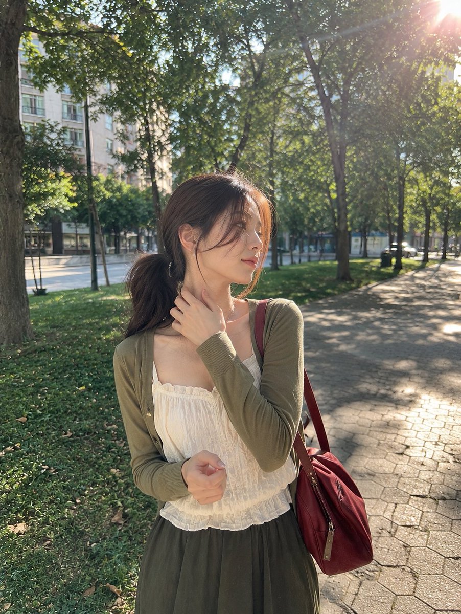 一张照片般逼真的抓拍户外肖像，画面中一位年轻女子在晴朗的午后站立于宁静的城市公园。她留着一头深棕色长发，梳成松散的低马尾，几缕纤细的碎发轻柔地垂落在脸庞两侧。她目光柔和地望向侧方，神情平静而若...