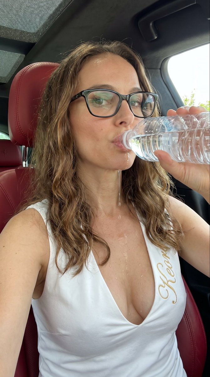年轻女性 Freya Allan，肤色白皙，长长的波浪状金色头发，黑框眼镜，绿色眼影，饱满的嘴唇含着水瓶口，眼神望向镜头, 长长的波浪状金色头发，稍显凌乱且蓬松, 身材曲线玲珑，胸部丰满显眼，...